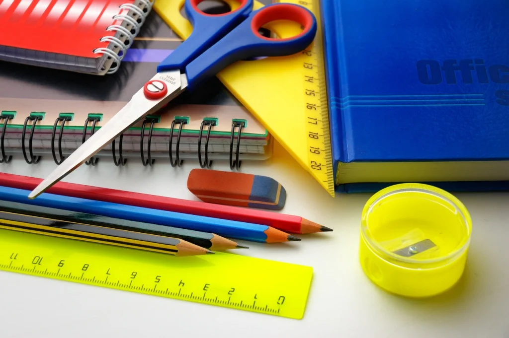 This image shows different classroom items like scissors, a ruler, different pencils, a sharpener, and notebooks.