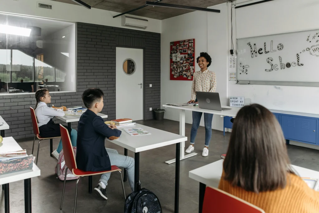 A teacher smiles and stands in front of her students in a classroom.
