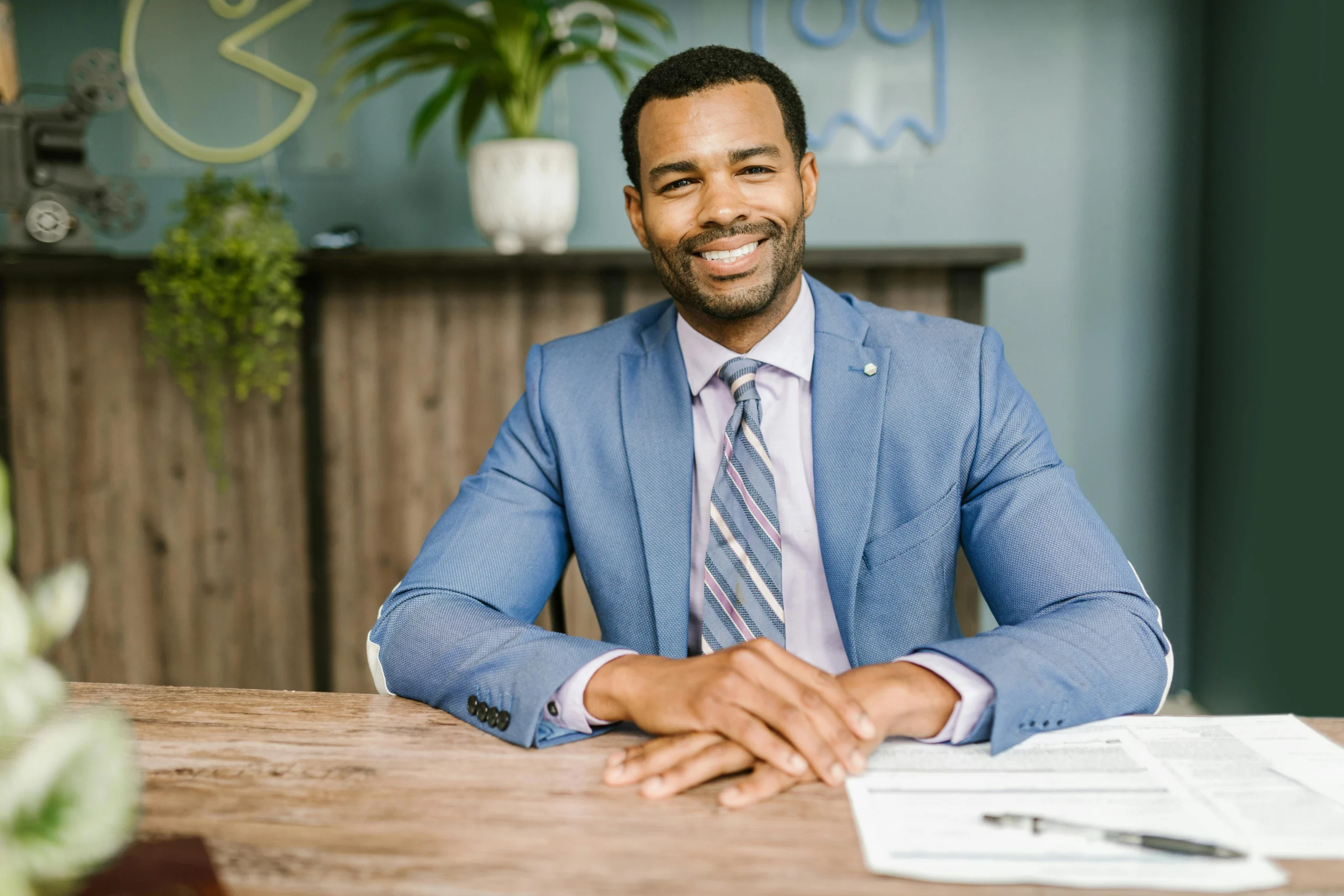A man in a suit smiles with his hands crossed over his desk.