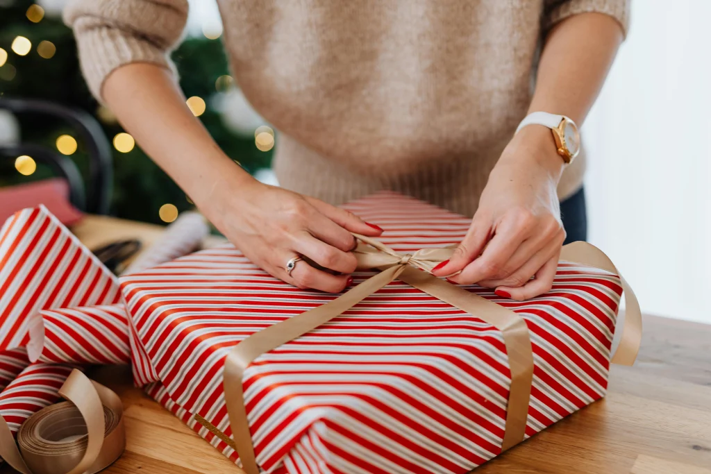 This picture shows a box being wrapped with Christmas gift wrapping paper and a golden ribbon.